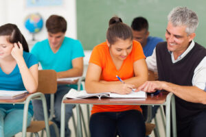 middle aged high school teacher helping a student in classroom