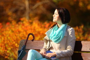 Fall lifestyle concept, harmony freedom. Casual young woman girl relaxing in autumnal park sitting on bench with book having fun, closed eyes. Golden colorful leaves background