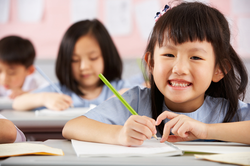 Group Of Students Working At Desks In Chinese School Classroom