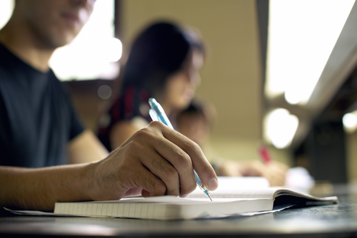 Students doing homework and preparing exam at university, closeup of young man writing in college library